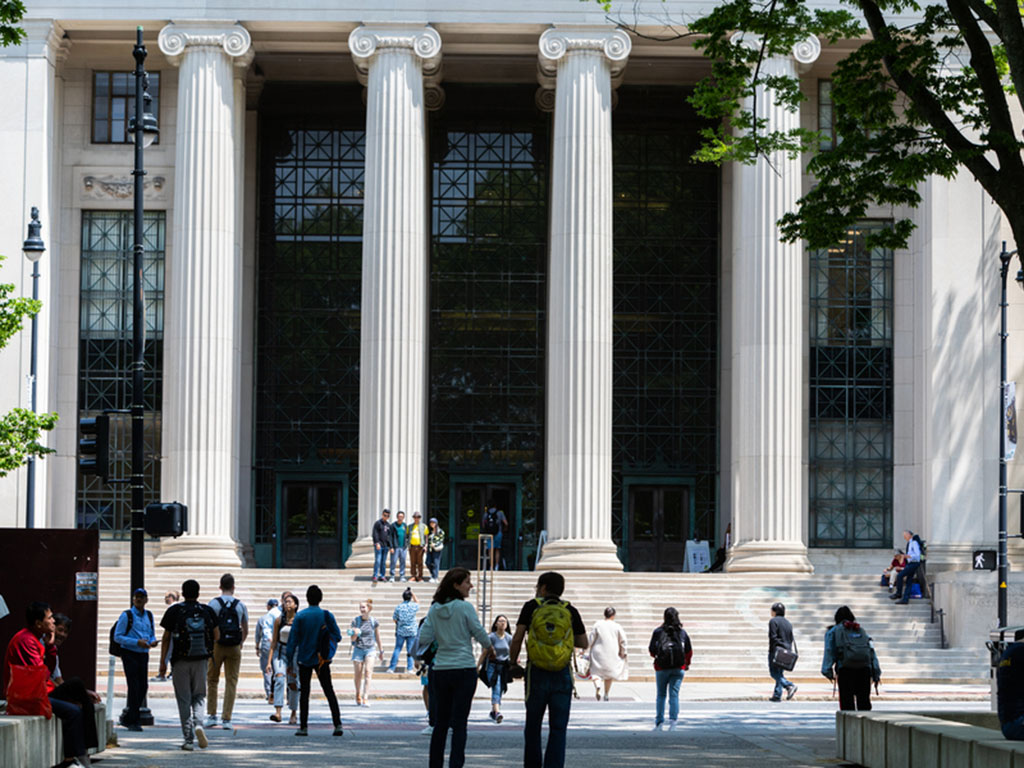 A building photo of the MIT campus, visitors cross the street at 77 Mass Ave